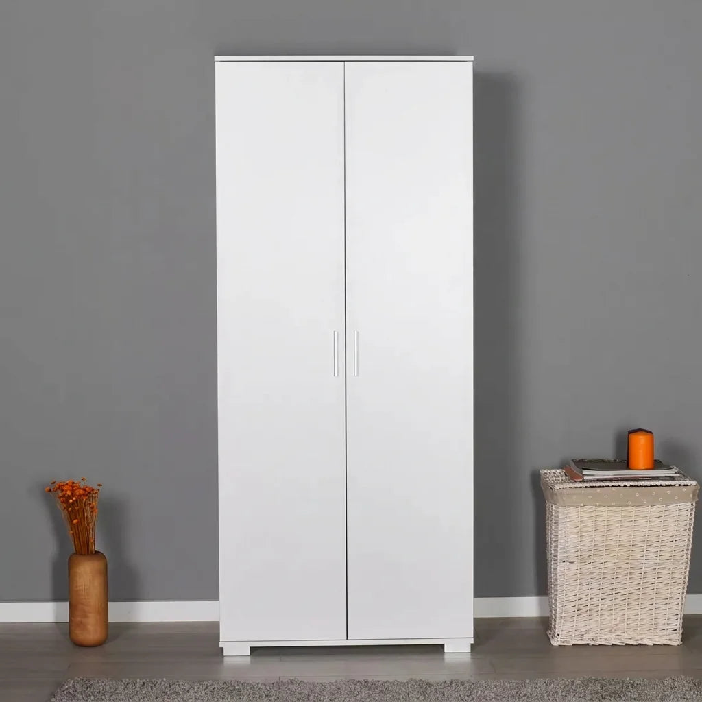 A tall white two-door wardrobe or armoire stands against a gray wall in a styled room. A woven basket sits on the right with a small orange candle on top, and a brown vase with dried orange stems sits on the left.