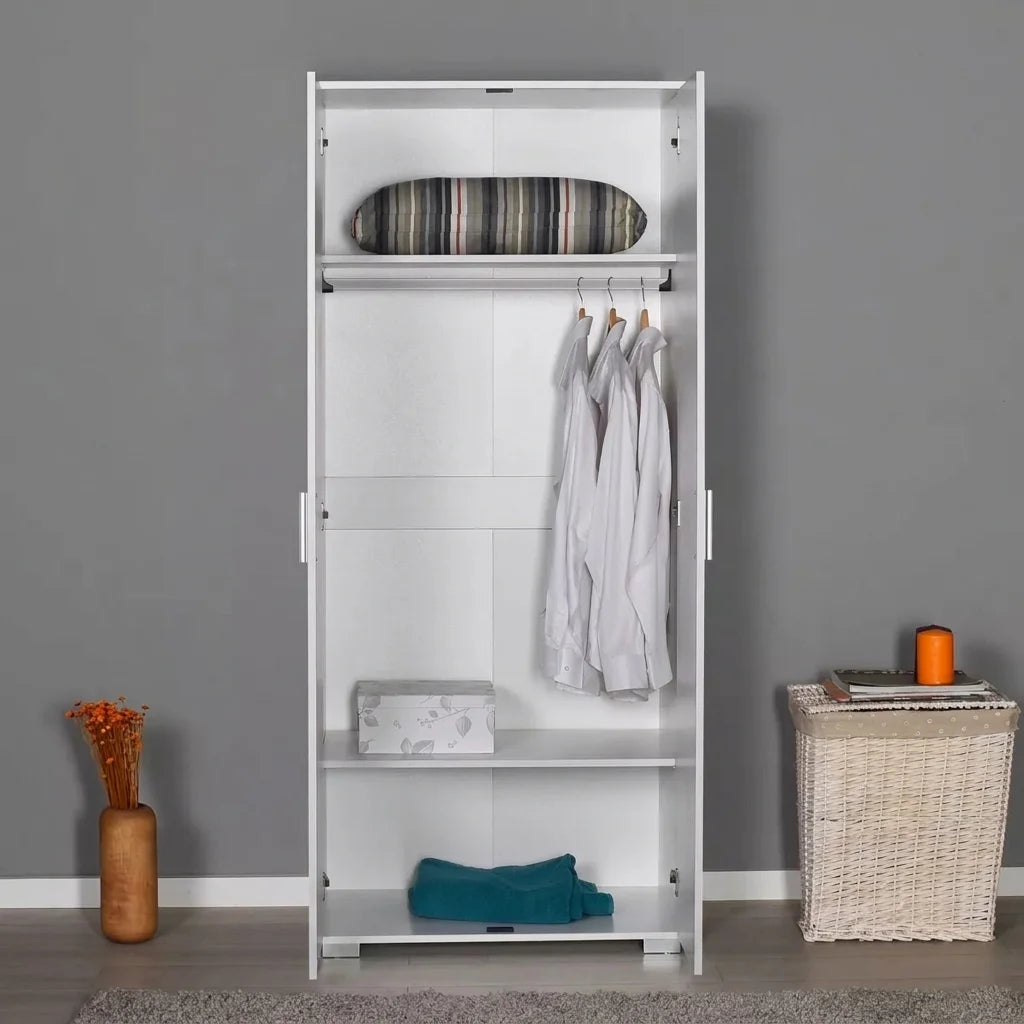 A tall white modular wardrobe or closet organizer with two doors, shown open in a styled room. The wardrobe has a top shelf with a striped cushion, a hanging rod with three white shirts, a middle shelf with a small box, and a bottom shelf with a folded teal blanket.